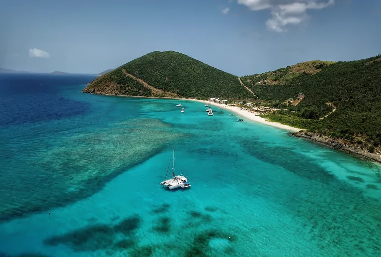 Aerial of a catamaran anchored in a turquoise reef bay below green hills