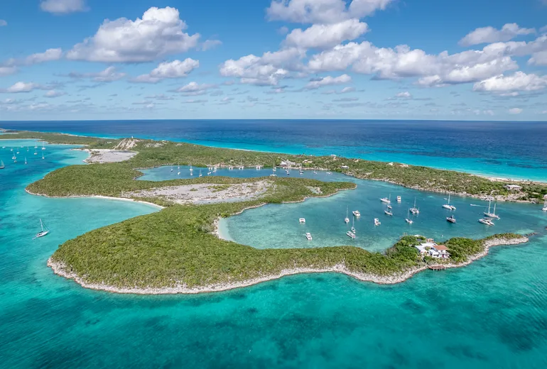 Aerial of a low reef-ringed cay with an inner lagoon and anchored yachts