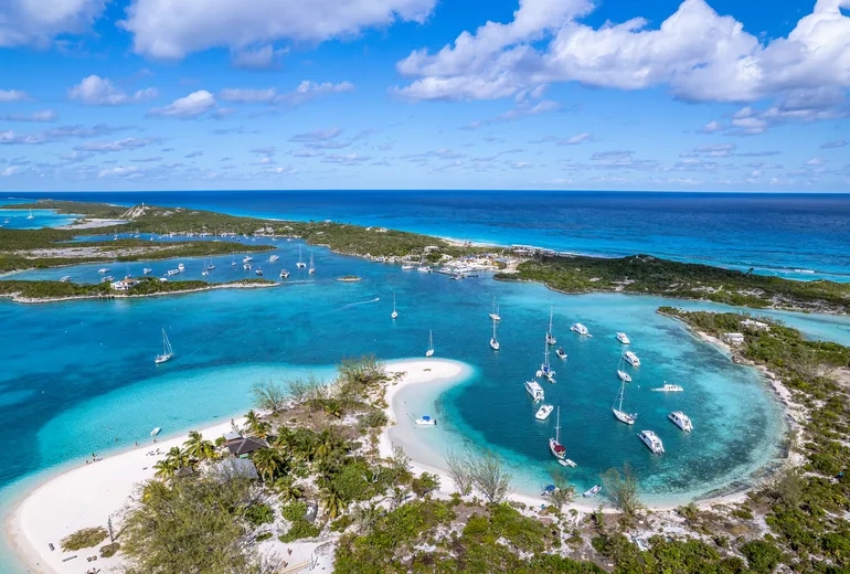 Aerial of a sandbar beach and busy turquoise anchorage filled with sailboats in the Bahamas cays