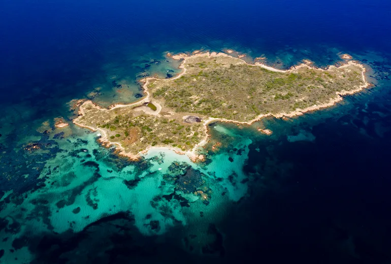 Aerial of a small rocky islet ringed by turquoise reef shallows