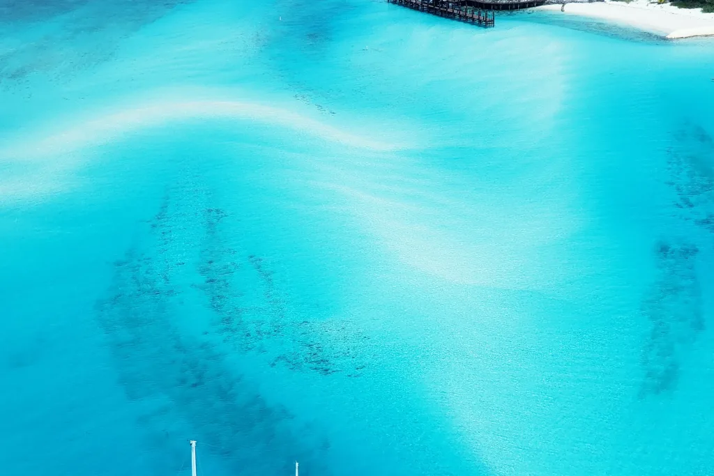 Aerial of lone sailboat over swirling turquoise sandbanks near small cay