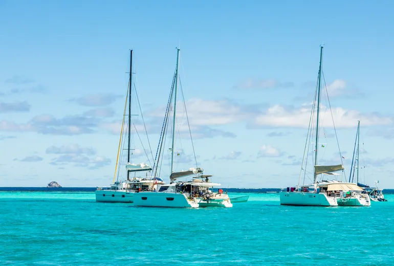Charter catamarans anchored in shallow turquoise water near a reef