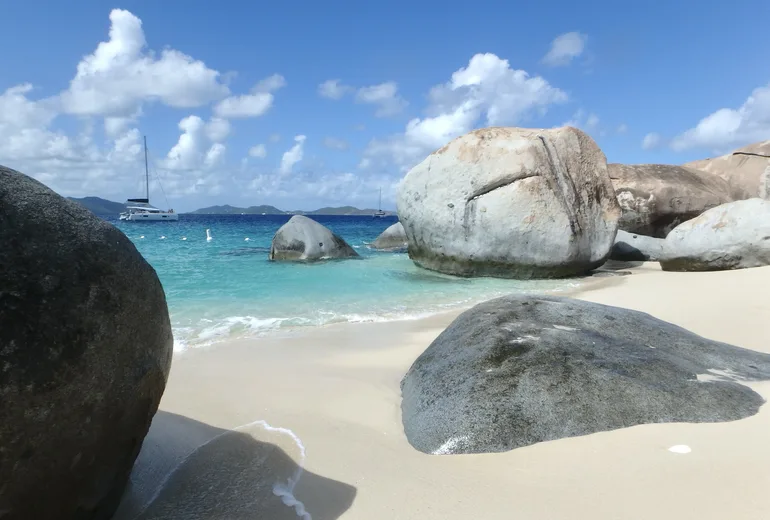 Granite boulders of The Baths on Virgin Gorda with a catamaran anchored offshore