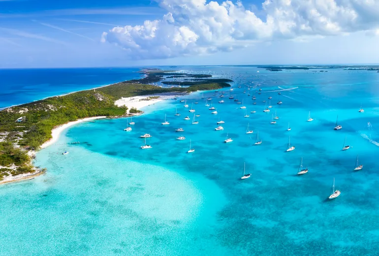 Panoramic aerial of sailboats anchored on turquoise banks along a low green cay