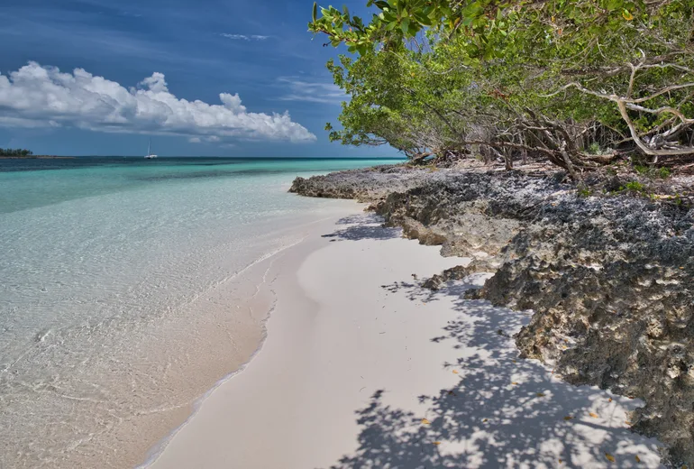 Quiet white sand shore with limestone rocks and a distant catamaran