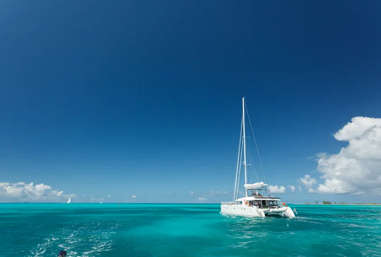 Sailing catamaran with guests cruising turquoise shallow banks under blue sky