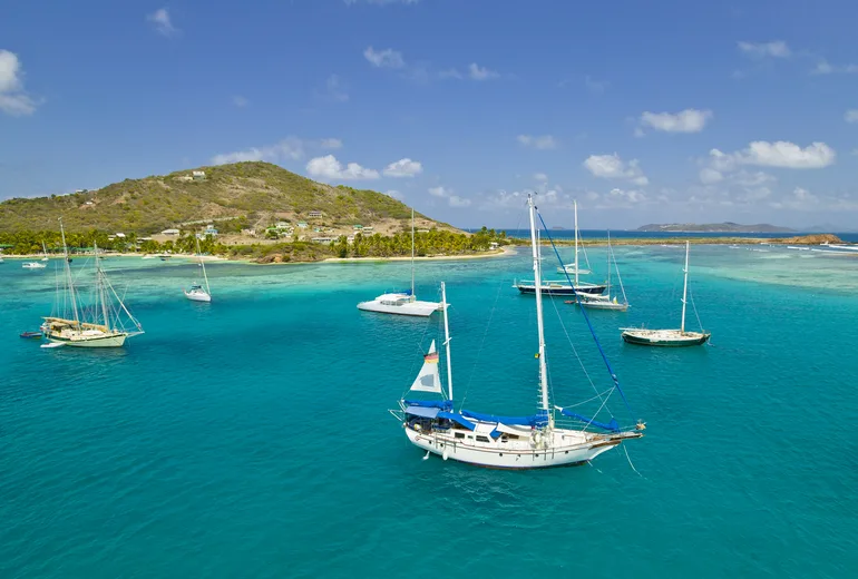 Sailing yachts anchored in a turquoise reef lagoon off a palm-fringed island