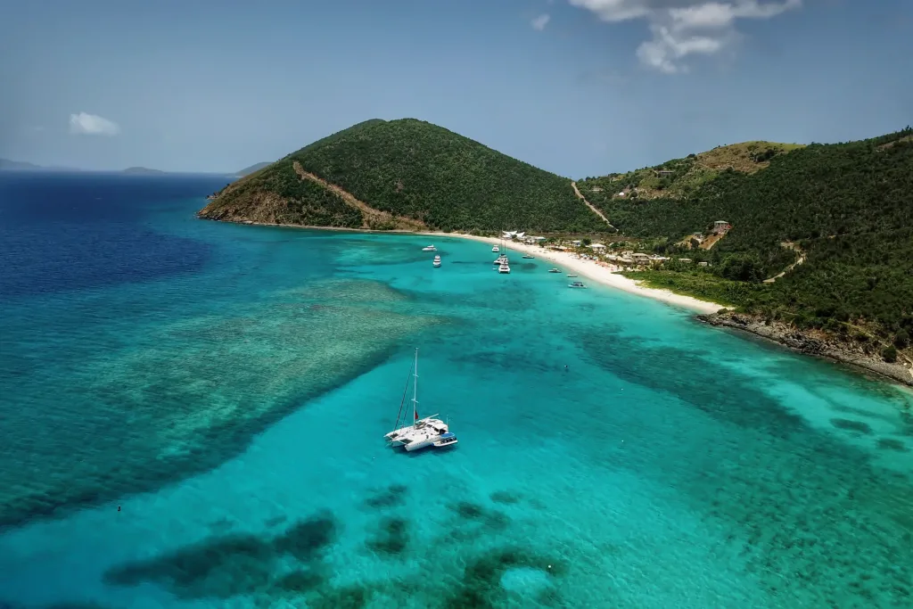 Aerial of catamaran anchored in turquoise reef bay below steep green hills and white beach
